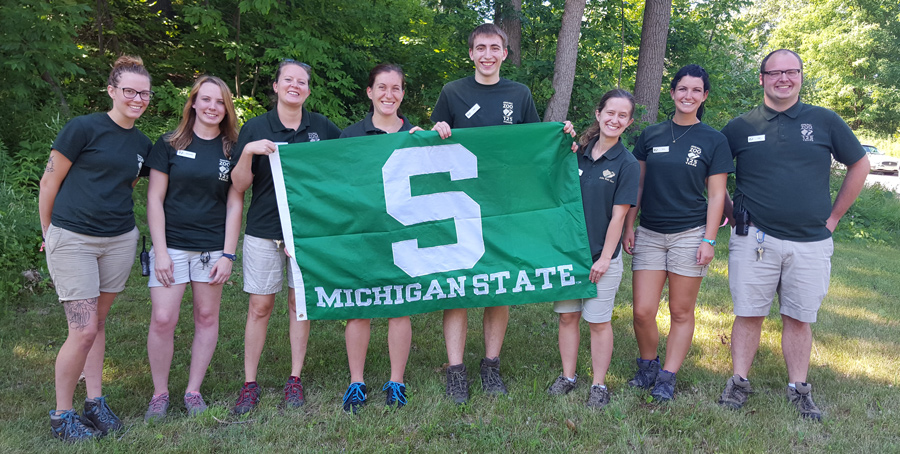 MSU students and alumni working at the John Ball Zoo holding an MSU flag